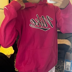 Rosa Nike hoodie med stor logga - Säljer den här nike hoodien då jag inte använt på länge och den ligger bara i garderoben 24/7. Snörning till huvan saknas men annars är den varm o perfekt till vintern. Storleken är L men för mig som brukar ha S/xs passar den ändå bra (lite stor). För mer funderingar/bilder skriv pm🫶🏻
