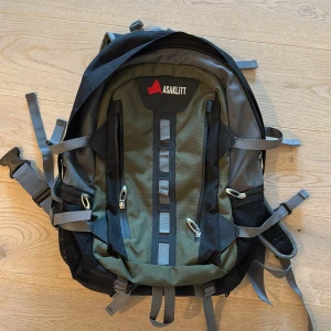 Grön och svart ryggsäck från Asaklitt - Ryggsäck med cool outdoor-look från Asaklitt i grön och svart polyester. Flera fack med dragkedja, meshfickor på sidorna och justerbara remmar för extra komfort. Perfekt för äventyr, skola eller träning. Snygg logga framtill och smarta detaljer för att fästa utrustning.