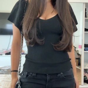 Svart ribbad topp från ONLY - Svart ribbad topp från ONLY med v-ringning både fram och bak. Toppen har korta, lite fladdriga ärmar och sitter snyggt figurnära. Perfekt att styla med jeans eller kjol för en clean look. Aldrig använt 💕