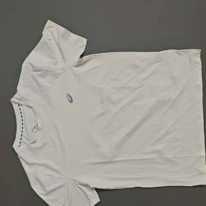 Vit t-shirt från Asics - Fräsch vit t-shirt från Asics med diskret logga på bröstet. Klassisk rund hals och korta ärmar. Perfekt för träning eller chill dagar. Materialet känns lätt och andas bra, vilket gör den skön att ha på sig när du är aktiv.