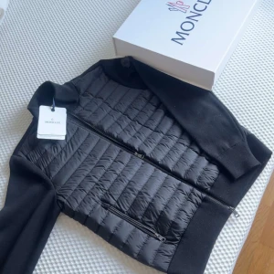 Moncler Cardigan - Snygg svart pufferjacka från Moncler med quiltad framsida och släta ärmar. Jackan har två dragkedjeförsedda fickor, hög krage och Moncler-logga på ärmen. 100% ÄKTA CERTIFIKAT OCH ALLT FINNS. Priset kan diskuteras.