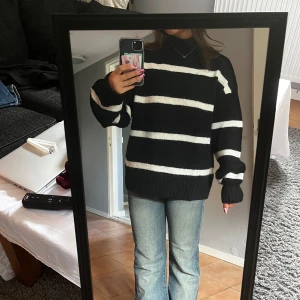 Svartvit randig stickad tröja - Intressekoll på denna svarta stickade tröja med breda vita ränder. Tröjan har en loose passform, långärmade ärmar och hög hals. Perfekt för dig som gillar en chill och stilren look. Passar till jeans eller kjol för en enkel outfit.