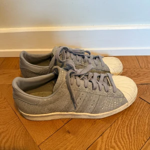 Grå/Blå Adidas Superstar sneakers, strl 40 - Säljer ett par grå/blå Adidas Originals Women's Snakeskin Superstar Sneakers. Använd fåtal gånger. Strl 40