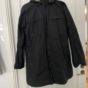 Peak Performance svart vinterjacka storlek L - Peak Performance svart vinterjacka i storlek L med avtagbar huva och dragkedja framtill. Innerjackan är avtagbar och båda jackorna kan användas separat. Jackan är lång, har praktiska fickor och är perfekt för kalla dagar. Insidan har ett rutigt foder i beige, svart och grått. Snygg och funktionell för höst och vinter. 