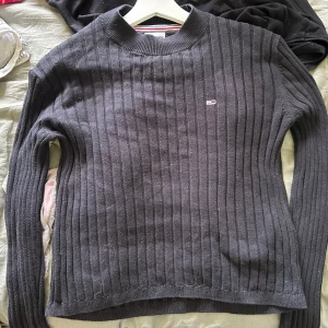 Mörkblå ribbad tröja Tommy Hilfiger - Snygg mörkgrå stickad tröja från Tommy Hilfiger med diskret logga på bröstet. Tröjan har ett ribbat mönster och rund hals, samt långa ärmar. Perfekt för dig som gillar klassisk stil med en modern touch.