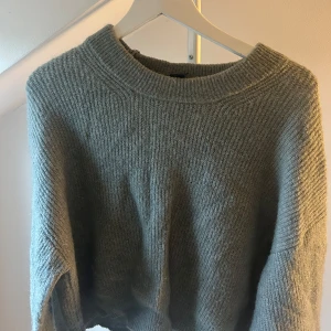 Grå/grön stickad tröja med rund hals - Mysig grå/grön stickad tröja med rund hals och långa ärmar. Tröjan har en loose passform och ribbad kant vid halsen, perfekt för att hålla värmen under kyliga dagar. Enkel och stilren design som funkar till jeans eller kjol.