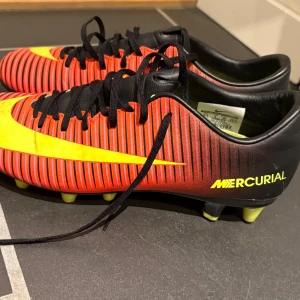 Nike Mercurial fotbollsskor röd/gul - Nike Mercurial fotbollsskor i rött och svart med gula detaljer och snörning.. Sparsamt använda. Strl 39