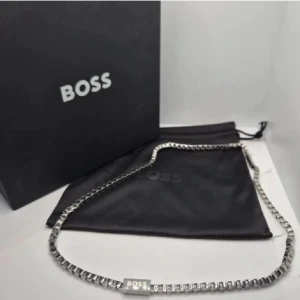 Silver halsband från BOSS - Stilrent silverfärgat halsband från BOSS med rektangulära länkar och en platta med BOSS-loggan. Kommer med original ask och tygpåse, perfekt för dig som gillar minimalistisk och modern design.