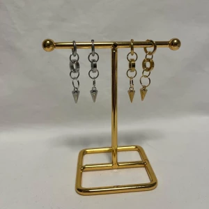 Chunky örhängen med kedjor och spikes - Säljer två par coola örhängen med chunky kedjor och spetsiga spikes. Ena paret är i blankt silverfärgat metall och det andra i guld. Perfekt för dig som gillar edgy och trendiga accessoarer. Passar till streetstyle och ger din look extra attityd.