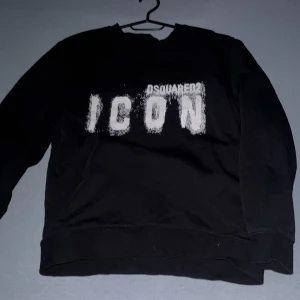 Svart sweatshirt Dsquared2 ICON M - Svart sweatshirt från Dsquared2 i storlek M med stor vit 'ICON' print på bröstet och Dsquared2-logga ovanför. Tröjan har rund hals, långa ärmar och ribbade muddar. Materialet är mjuk bomull som känns skön mot huden. Perfekt för dig som gillar streetwear och vill sticka ut.