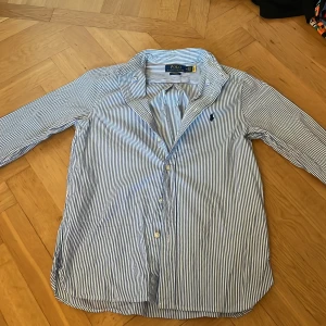 Randig skjorta från Polo Ralph Lauren - Snygg blåvit randig skjorta från Polo Ralph Lauren i slim fit-modell. Skjortan har klassisk krage, långa ärmar och knäppning framtill. Broderad logga på bröstet och tillverkad i mjuk bomull. Perfekt för en clean och stilren look.