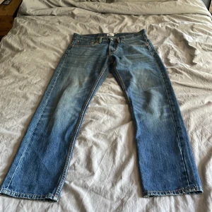 Blå jeans från 157 med raka ben - Säljer ett par klassiska blå jeans från 157 med raka ben och fem fickor. Jeansen har en brun läderpatch bak i midjan och snygga kontrastsömmar. Modellen är straight fit och tillverkad i slitstarkt denimtyg. Storlek W31 L30.                             
