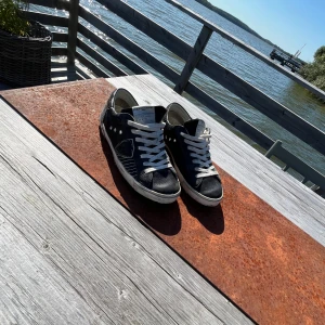 Svarta Philippe Models  - Snygga svarta sneakers från Philippe Model med vita snören och vit sula. Skorna har rund tå och coola detaljer på sidan samt märkets logga under sulan. Materialet är skinn och insidan är ljus. Perfekta för dig som gillar streetstyle och vill ha något unikt på fötterna.