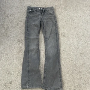 Grå bootcut jeans från Gina Tricot - Säljer ett par grå jeans från Gina Tricot i storlek 164. Modellen är bootcut med snygga detaljer på bakfickorna, inklusive mönstrade kanter och silvriga knappar. Jeansen har klassisk femficksdesign och är tillverkade i jeansmaterial med en cool tvättad look. 💞