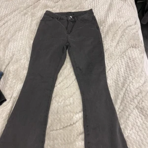 Mörkgrå bootcut jeans från Vila - Snygga mörkgrå jeans från Vila i bootcut-modell med hög midja. Klassisk femficksdesign och knappstängning framtill. Jeansen är tillverkade i ett mjukt bomullsmaterial med lite stretch för extra komfort. Perfekta för dig som gillar en retro vibe och vill ha ett par jeans med lite extra attityd.