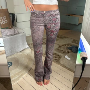 Mönstrade bootcut jeans i grått och rosa - Säljer ett par unika bootcut jeans med grå och rosa mönster. Byxorna har låg midja och klassisk femficksmodell. Materialet är jeans och passformen är slim upptill med utsvängda ben. Perfekta för dig som vill sticka ut med coola detaljer.