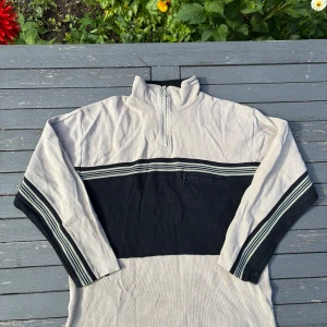 Beige och svart half zip tröja Bruno Altonelli - Säljer en beige och svart långärmad tröja från Bruno Altonelli med half zip och ståkrage. Tröjan har breda svarta ränder över bröstet och ärmarna, samt en liten ficka med dragkedja på framsidan. Materialet är ribbad bomull för en chill och skön känsla.