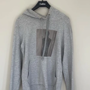Grå hoodie med konstnärligt tryck - Grå hoodie med konstnärligt tryck på bröstet. Trycket har försvunnit en del som man kan se på bilderna! finns även smink fläck men dä syns inte utanpå!💗