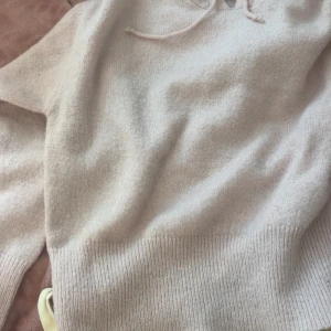 Rosa stickad hoodie med snörning - Mysig rosa stickad hoodie med snörning vid halsen. Tröjan har långärmade och ribbade muddar vid ärmslut och nederkant. Perfekt för dig som gillar en enkel och chill stil med ljusa färger.