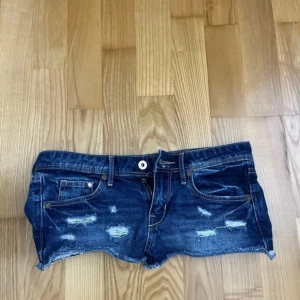 Mörkblå jeansshorts med slitningar - Snygga mörkblå jeansshorts med rå kant och slitna detaljer framtill. Klassisk femficksmodell med knapp och dragkedja. Perfekta för en chill sommarlook och passar dig som gillar streetstyle.