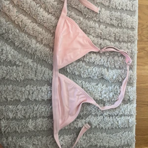 Ljusrosa bikiniöverdel med knyt - Snygg ljusrosa bikiniöverdel med klassisk trekantsform och justerbara axelband. Den har ett smidigt spänne i ryggen och tunna band för att knyta runt halsen. Materialet är mjukt och stretchigt, perfekt för strandhäng och poolparty.