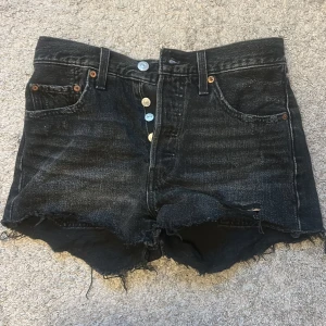 Svarta jeansshorts från Levi's Premium - Svarta jeansshorts från Levi's Premium, fransiga kanter. Klassisk femficksdesign, knappar framtill. Snyggt slitna detaljer och cool vintage vibe, perfekta för sommaren. Inte andvänd många gånger!❤️❤️