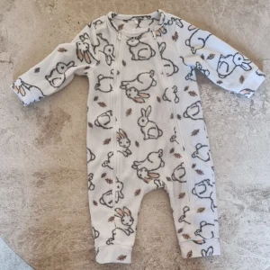 Fleecebyxdress med kaniner Cool Club - Supermjuk vit fleecebyxdress från Cool Club i storlek 68 med gulligt kaninmönster. Dubbla dragkedjor framtill gör den enkel att ta på och av. Perfekt för hösten eller som ett mellanlager under kyliga dagar. 