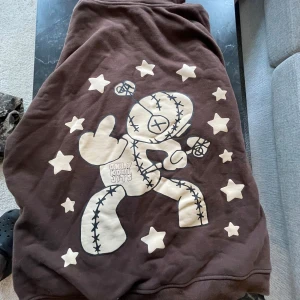 Brun hoodie Only Kool Jits - Säljer en brun hoodie från Only Kool Jits med stor grafisk print på ryggen av en tecknad figur omgiven av stjärnor och texten 'ONLY KOOL JITS' på framsidan. Hoodien har huva och känguruficka, trycket är i beige och ger en unik streetwear-vibe.