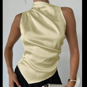 Champagnefärgad siden polotopp - Aldrig använd💕Supersnygg polotopp i champagnefärgat siden med ärmlös design och asymmetrisk nederkant. Perfekt för dig som gillar en clean och lyxig vibe. Toppen har en hög krage och sitter riktigt snyggt mot kroppen. 