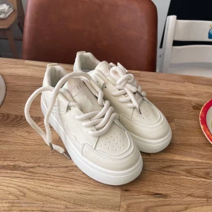 Vita sneakers med plattform  - Snygga vita sneakers med chunky plattformssula och rund tå. Skorna har breda, vita snören och perforerade detaljer på tån för extra stil. Perfekta för dig som gillar clean och modern look.Helt nya