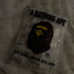 BAPE Shark Camo Hoodie i beige M - Säljer en BAPE Shark Hoodie i vit och grå camo med ikonisk hajdesign på huvan och broderade detaljer. Den är inte använd och är nyköpt och du får med påsen. Hoodien har dragkedja, ribbade muddar och klassisk BAPE-logga. Perfekt för dig som vill sticka ut med streetwear från ett av världens mest hypade märken.