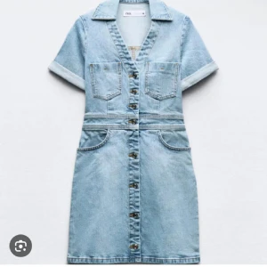 Jeansklänning med knappar från Zara - Snygg ljusblå jeansklänning från Zara med korta ärmar, v-ringning och krage. Klänningen har framfickor på bröstet och höften samt knappar hela vägen framtill. Perfekt för dig som gillar en avslappnad och cool stil.