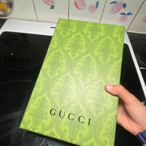Brun axelväska från Gucci - Snygg brun keps från Gucci med klassiskt GG-mönster i beige och brunt. Kepsen har detaljer i brunt skinn och dragkedja upptill. Insidan är ljus och har en etikett med Gucci-logga. Perfekt för dig som vill ha en ikonisk designeraccessoar.