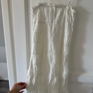 Vit kort klänning från H&M Divided - Supersöt vit klänning från H&M Divided i storlek XXS. Klänningen har tunna axelband, rynkad överdel med volangkant och ett lätt, luftigt tyg i bomull. Perfekt för varma dagar och har en avslappnad, flowy passform som känns riktigt fräsch.