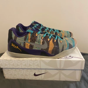 Nike Kobe 9 low - Säljer ett par Nike Kobe 9 low sneakers med ett färgglatt mönster i blått, orange och lila. Skorna har snörning och en unik design som sticker ut. Perfekta för basket eller som statement piece i vardagen.