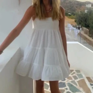 Vit sommarklänning med smockdetaljer - Söt vit klänning med smockdetaljer upptill och tunna axelband. Perfekt för varma sommardagar med sin luftiga design och korta längd. Klänningen har en avslappnad passform och är gjord i ett lätt material som ger en skön känsla.