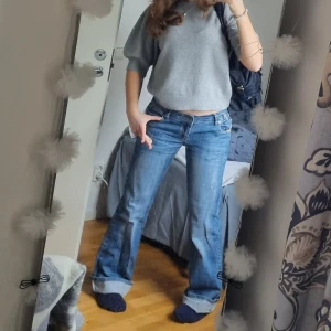 Blå jeans med broderade detaljer - Snygga blå jeans med broderade detaljer på bakfickorna. De har en klassisk femficksdesign och är uppvikta vid anklarna för en avslappnad look. Perfekta för en casual stil.