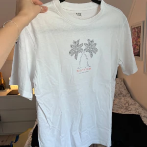 Vit t-shirt med palmtryck - Säljer en vit t-shirt från Lager157 med ett stilrent tryck av två palmer och texten 'The City of Palms, Fort Myers, Florida'. Perfekt för en avslappnad stil. T-shirten har ett liten fläck på framsidan (näst sista bilden), men knappt synlig. Oversized i storleken. Önskar du veta exakta mått? Tveka inte att höra av dig!