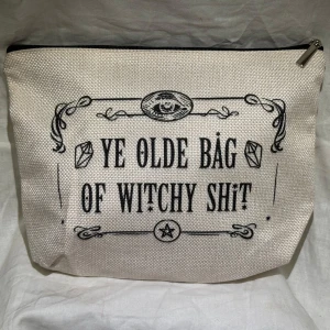 Ny! Beige necessär med text - Ny! Säljer en beige necessär med texten 'Ye Olde Bag of Witchy Shit' i svart. Väskan har en dragkedja upptill och är perfekt för att förvara småsaker. Den har en stilren design med dekorativa detaljer runt texten. Text på båda sidor. Kika gärna på mina andra annonser har massor att sälja 🌸