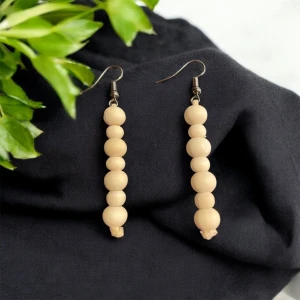 Beige örhängen med träpärlor - Snygga och stilrena örhängen med flera beige träpärlor på rad. Perfekta för att ge en naturlig touch till din outfit. De har en enkel krok för enkel användning.
