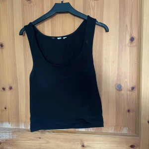 Svart linnetopp från H&M - Säljer en stilren svart linnetopp från H&M. Toppen har en enkel design med breda axelband och rund halsringning. Perfekt för lager-på-lager eller som den är under varma dagar. Lappen är borttagen men det är samma information som står på den lappen som finns i bilden.