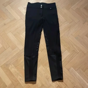 Svarta ridbyxor från CRW, Hööks - Snygga svarta halvskodda risbyxor med justerbar midja. Passar c. en 155 cm lång. Storlek 36. Stretchiga och sköna byxor. Säljes för att det blivit för små. Märke: CRW (Hööks).