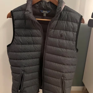 Grå väst från Polo Ralph Lauren - Säljer en snygg grå dunväst från Polo Ralph Lauren. Västen är använd en del men i perfekt skick. En minimal deffekt (se bild 5) men som inte syns vid användning. Säljer då jag växt ur den. 