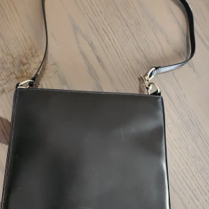 Svart axelväska från InWear - Snygg svart axelväska från InWear i ett stilrent och minimalistiskt design. Väskan har en justerbar axelrem och stängs med en tryckknapp. Perfekt för att bära dina nödvändigheter med stil.