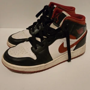 Nike Air Jordans i svart, vitt och rött - Säljer ett par klassiska Nike Air Jordans i svart, vitt och rött. Skorna har snörning och den ikoniska Air Jordan-loggan på sidan. Perfekta för dig som älskar sneakers med stil och komfort.
