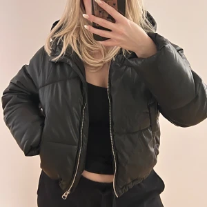 Svart pufferjacka med huva - Snygg svart pufferjacka med silverdetaljer och huva i storlek Small. Jackan är croppad och man kan justera nederkanten . Fläckar av smink finns på insidan av jackan men ej så synliga (se bild). Märket är bershka. Köparen står för frakten 🩷