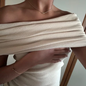 Beige offshoulder topp - Säljer en stilren beige offshoulder topp i ribbat material. Perfekt för en elegant look med sin axelbandslösa design. Passar bra till både jeans och kjol.