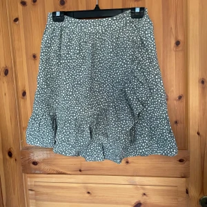 Grön prickig kjol från Vero Moda - Säljer en söt grön kjol med vita prickar från Vero Moda. Kjolen har en volangdetalj längst ner och en bekväm passform. Perfekt för en avslappnad stil.