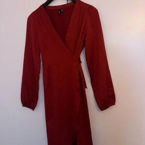 Vinröd omlottklänning - Snygg vinröd omlottklänning med långa ärmar och knytband i midjan.  Från vero Moda. 