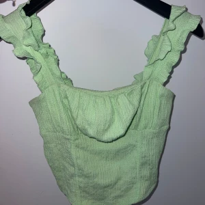 Grön topp med volangdetaljer - Säljer en söt grön topp med volangdetaljer på axelbanden. Från Gina tricot.